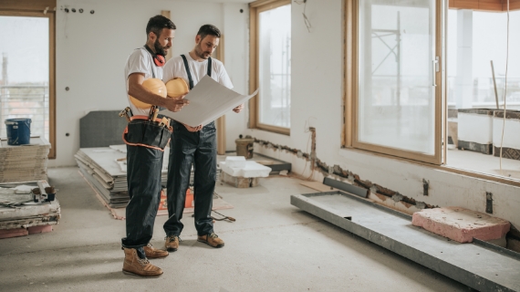 Sanierungsguide Handerwerker analysieren Plan auf der Baustelle.